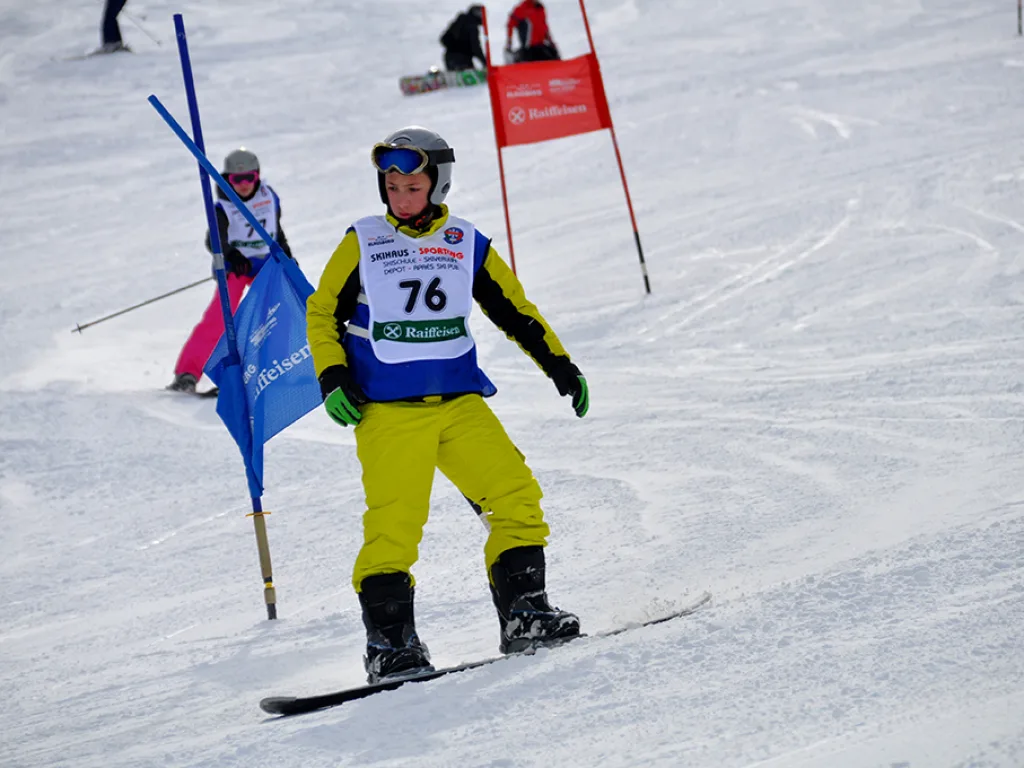 Snowboarder in gelber Hose mit Startnummer 76 auf der Strecke.